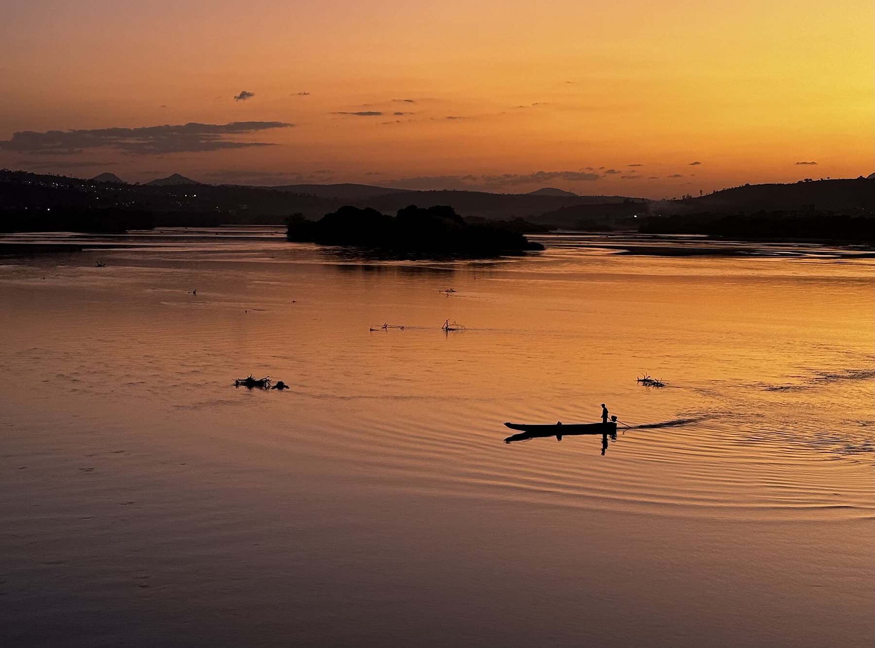 A lone fisherman paddling across a calm river at golden sunset