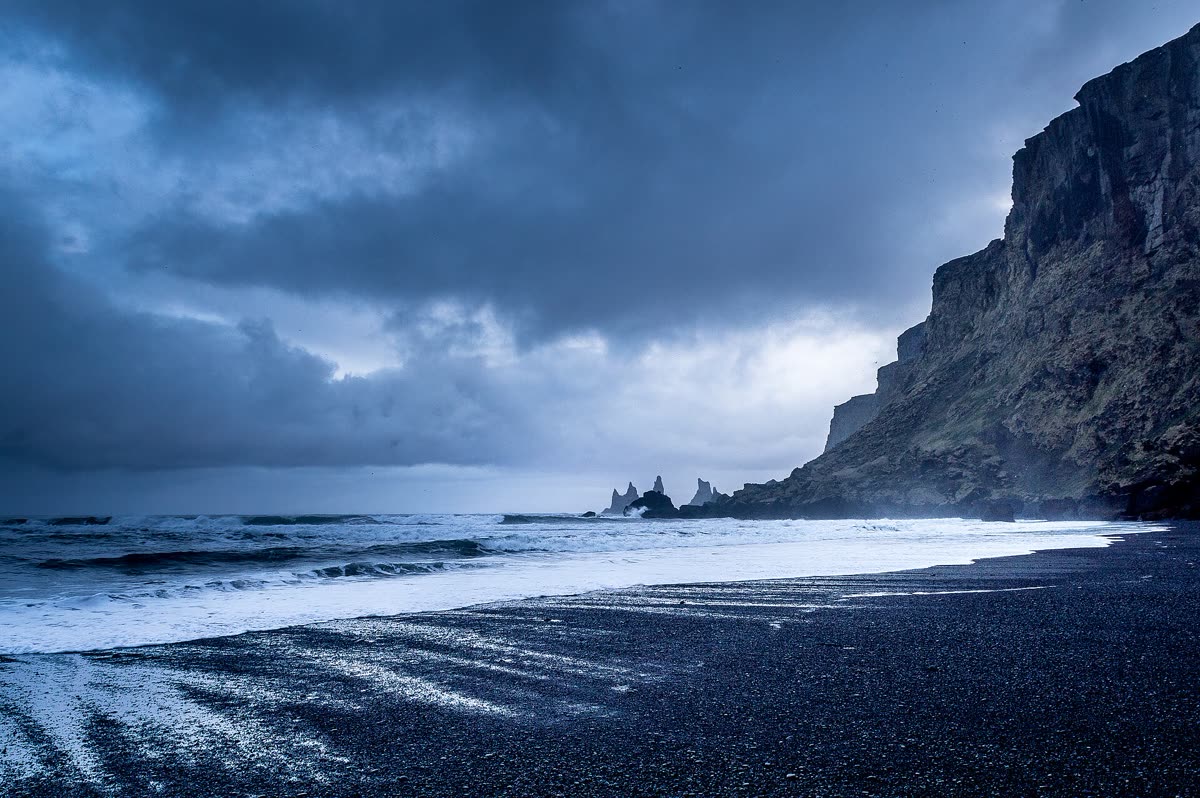 Storm clouds rolling over a black sand beach and dark cliffs